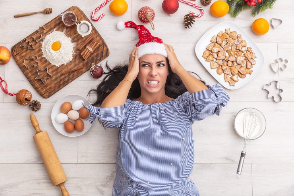 Woman wearing a Christmas hat with a frustrated expression, surrounded by baking ingredients and festive decorations.