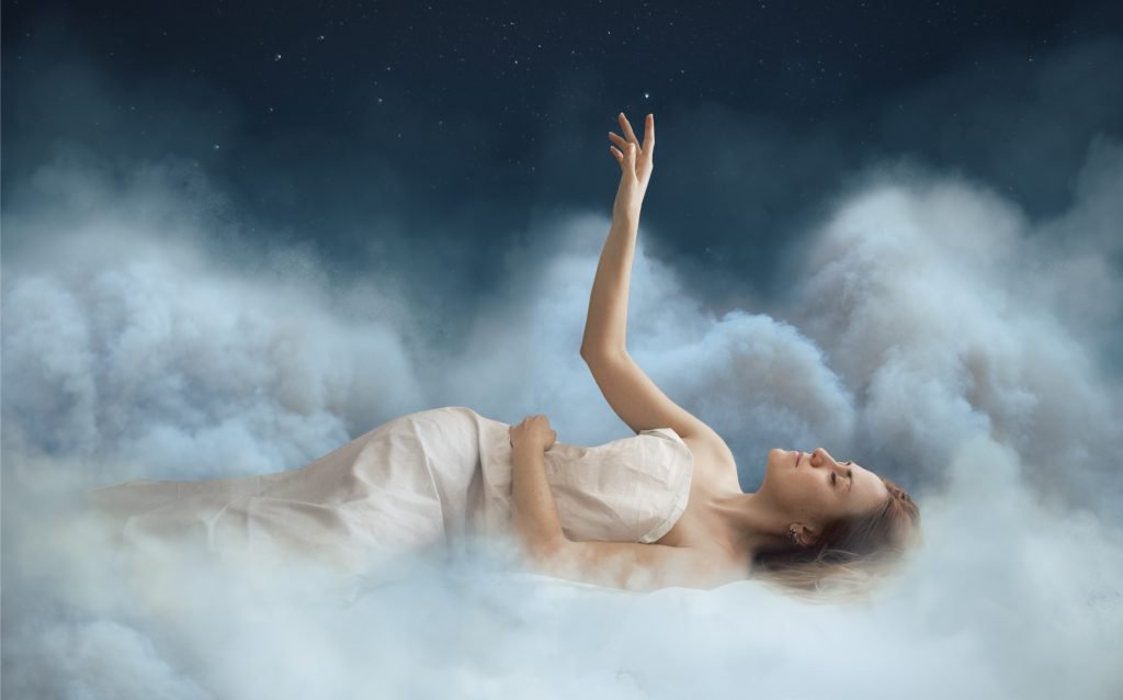 A girl lying on clouds with her hand reaching towards the stars in a dreamy night sky.