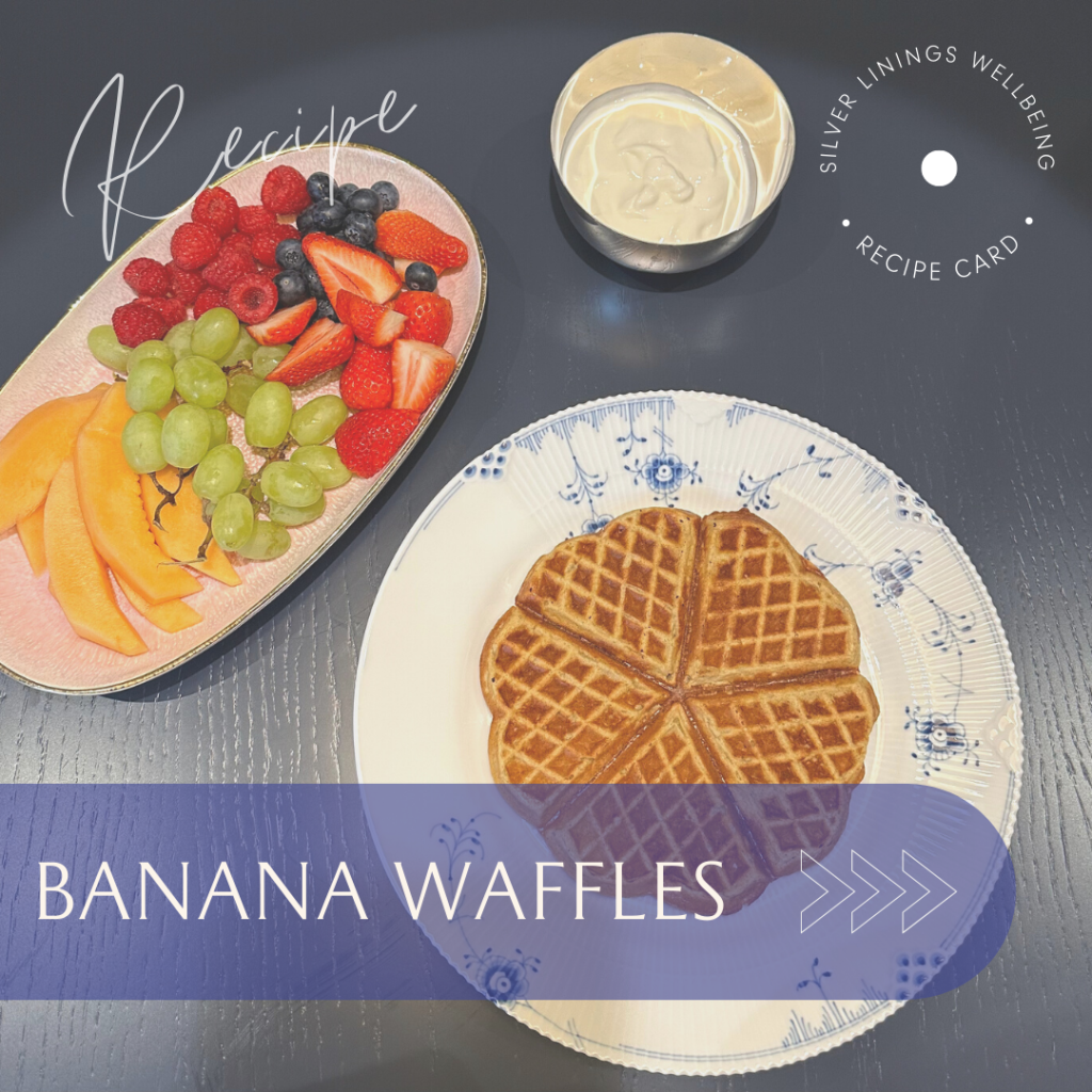 Plate of banana waffles accompanied by a selection of fresh fruits including grapes, berries, and melon.