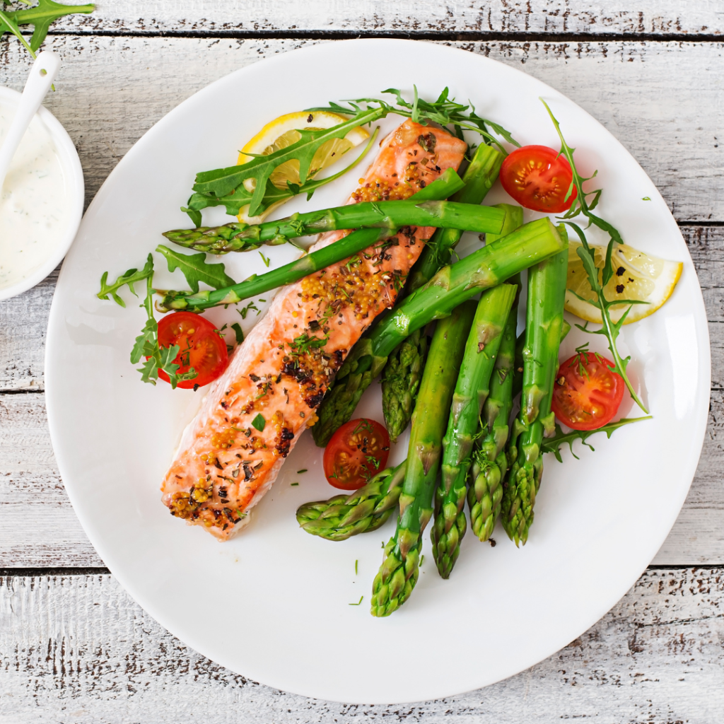 Plate of grilled salmon fillet served with asparagus, cherry tomatoes, and lemon slices on a rustic wooden table.