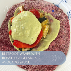 Beetroot wrap filled with roasted vegetables and topped with avocado sauce on a white plate.