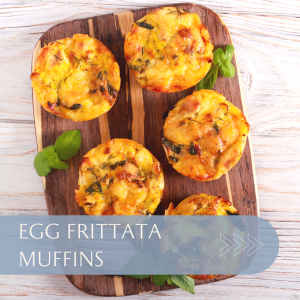 Five egg frittata muffins arranged on a wooden board with fresh herbs.