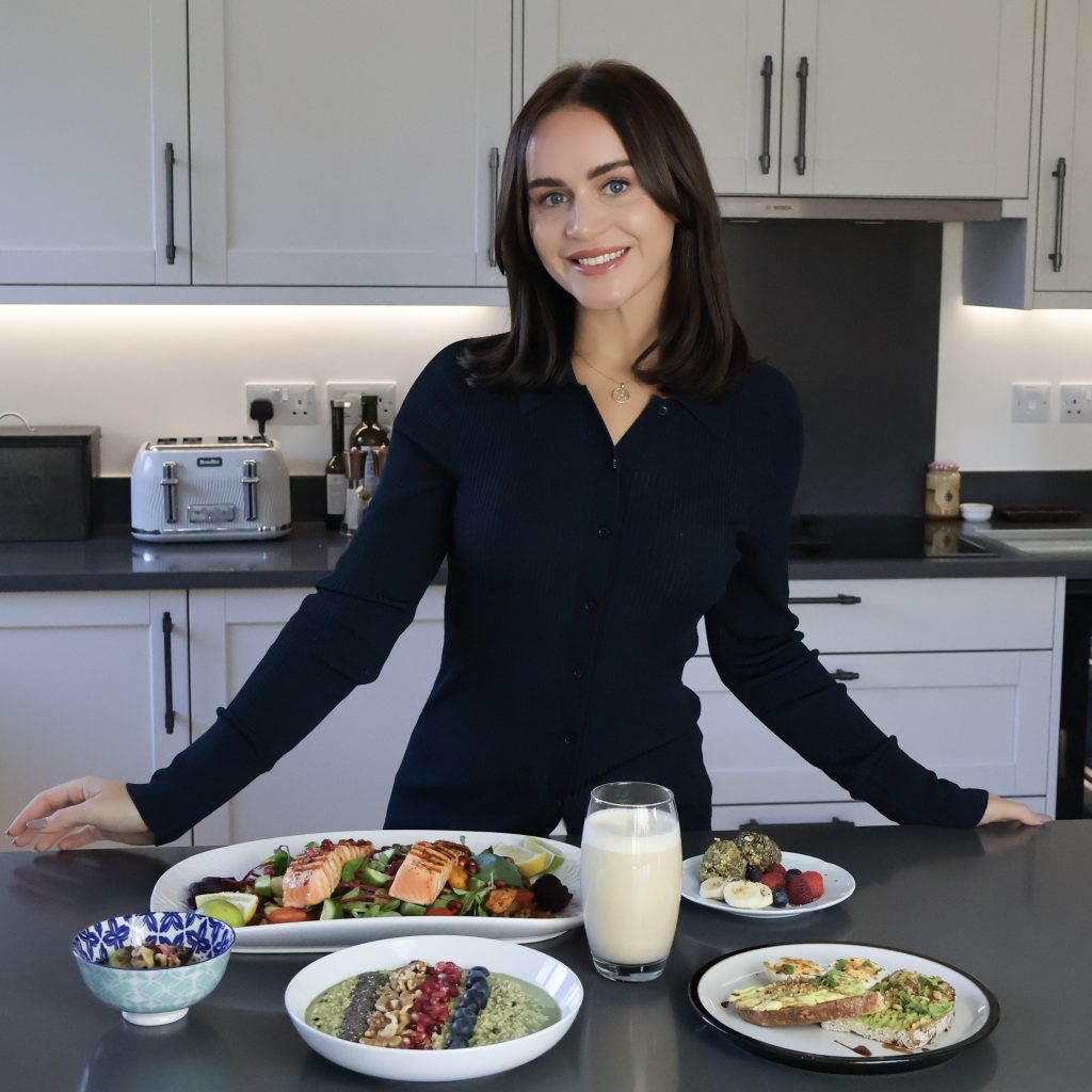 A woman standing in a kitchen with a variety of dishes including salmon, salads, and desserts on the table.