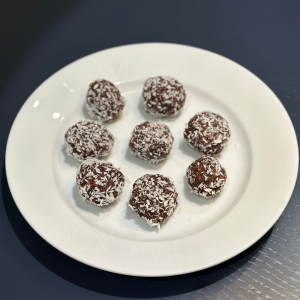 Nine choc cashew energy balls coated in desiccated coconut arranged on a white plate.