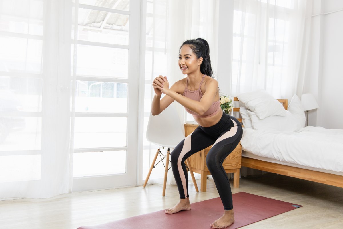 A woman in activewear performing squats on a yoga mat in a bright indoor space.
