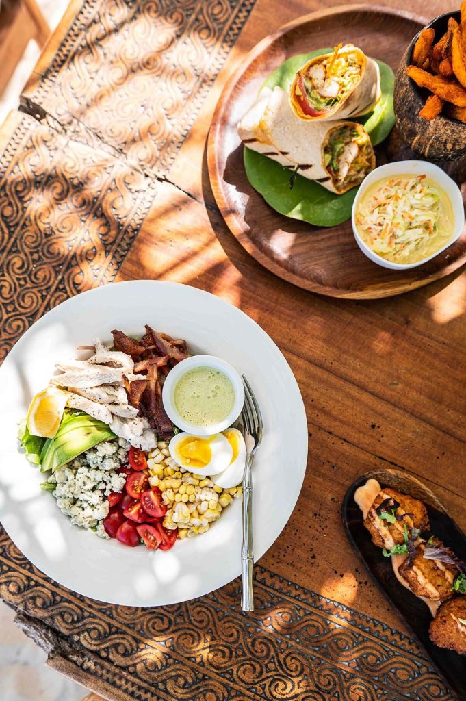 A bowl of salad featuring chicken, bacon, corn, tomatoes, and a boiled egg served with wraps and coleslaw.