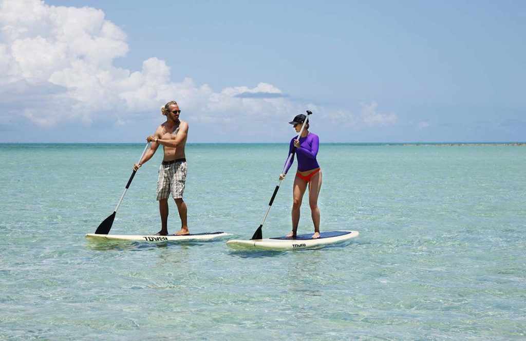 Two individuals paddling on stand-up paddle boards in clear turquoise water under a blue sky.