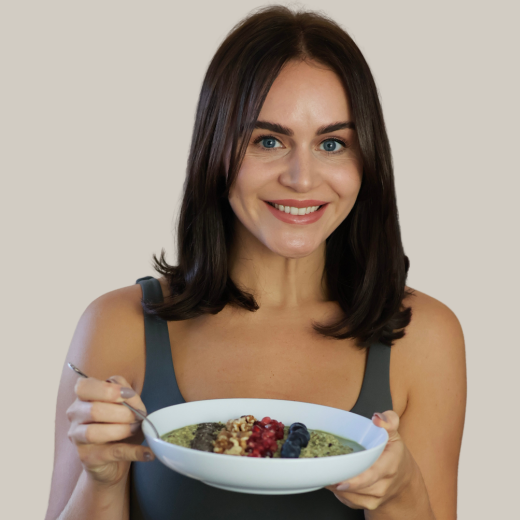 Woman smiling while holding a bowl of smoothie topped with nuts and berries.