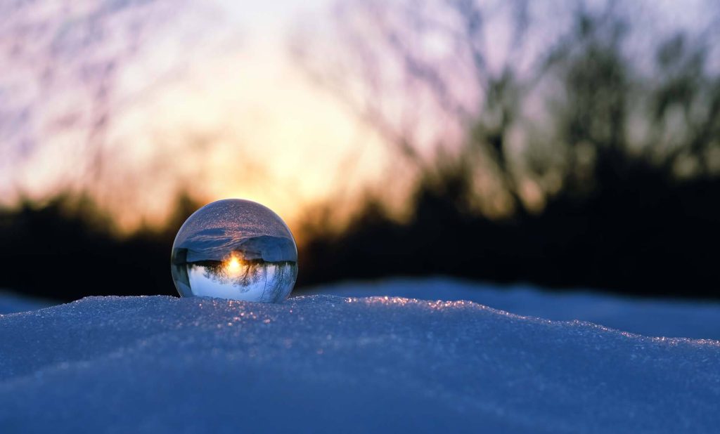 A glass sphere reflecting the sunset, resting on a layer of snow.