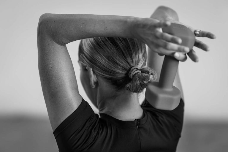 A woman performing an exercise with a dumbbell held behind her head, showcasing her arm and shoulder muscles.