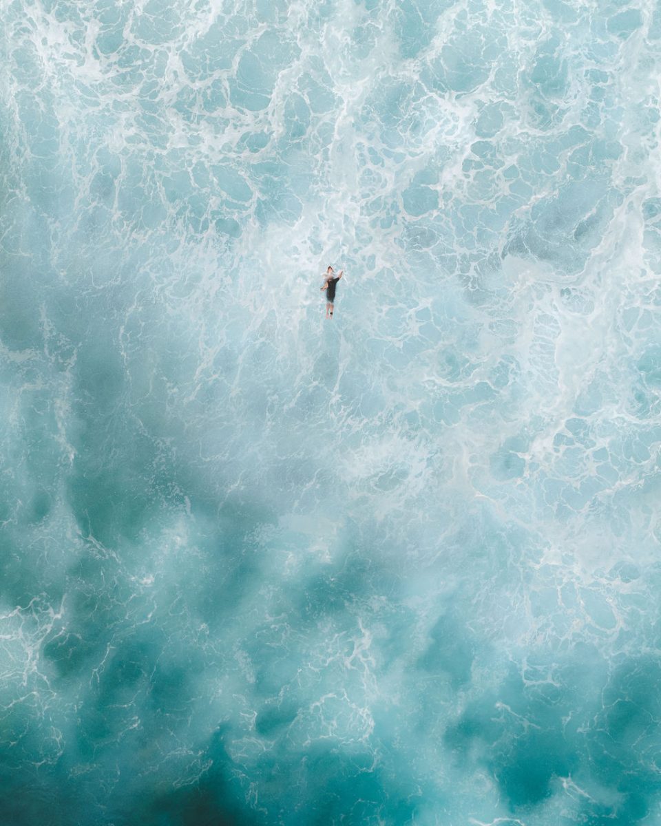 A person floating on the surface of ocean waves, surrounded by turquoise water and foam, 2 High.