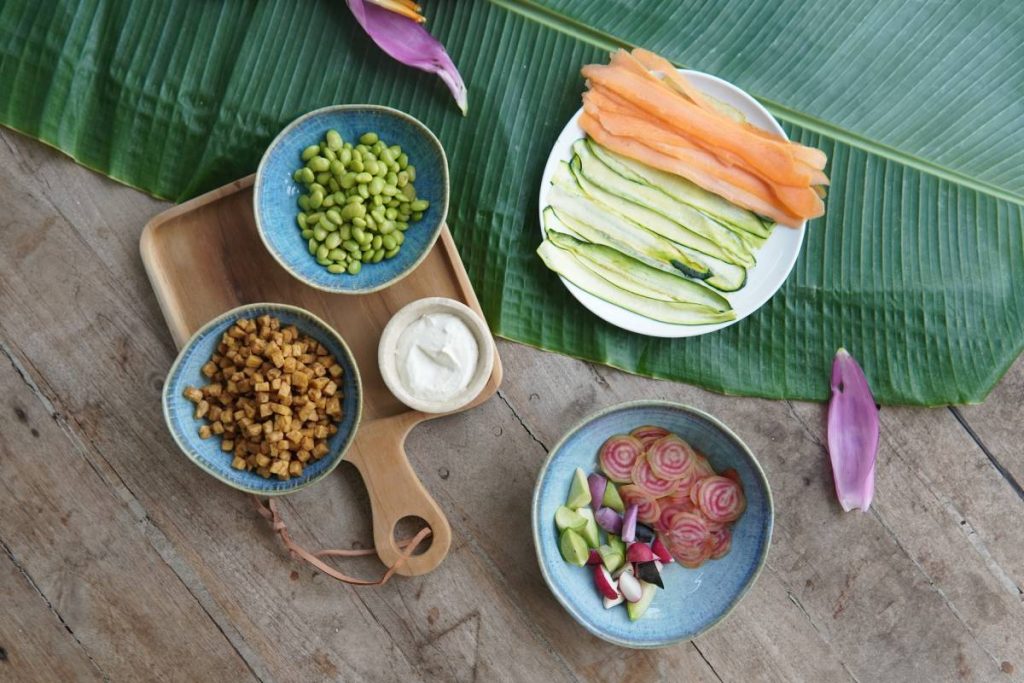 Bali bowl containing edamame, sliced vegetables, and miso dressing arranged on a wooden board.