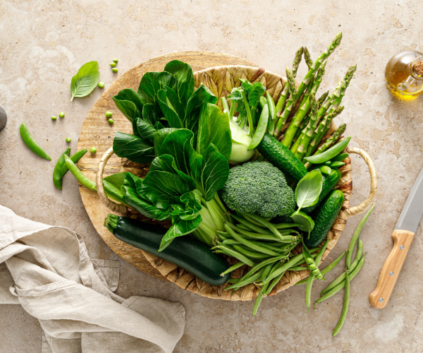 A variety of green vegetables including broccoli, asparagus, and cucumbers arranged in a woven basket.
