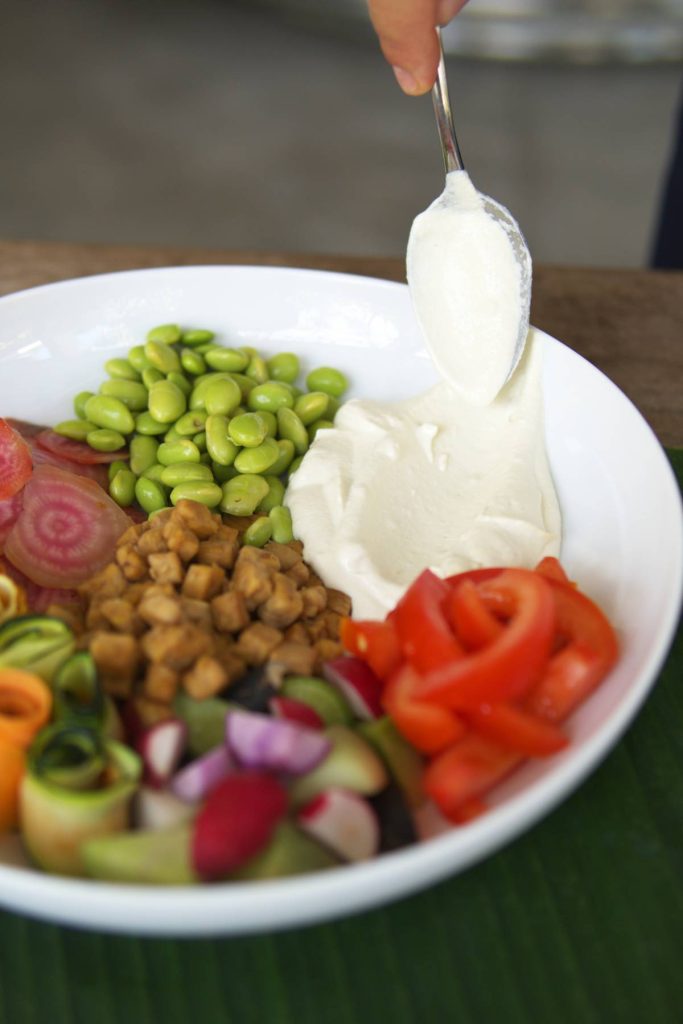 Bali bowl containing edamame, red peppers, radishes, and a dollop of miso dressing being added.