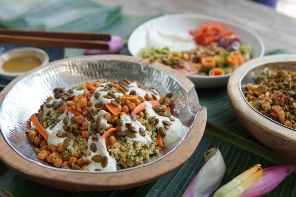 Quinoa salad topped with carrots, seeds, and miso dressing served in a wooden bowl.