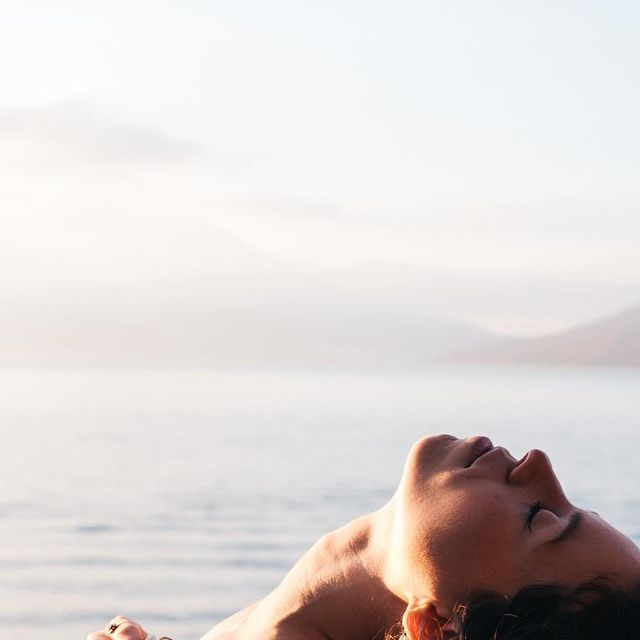 A woman lying back with her eyes closed, enjoying a moment of relaxation by the water.