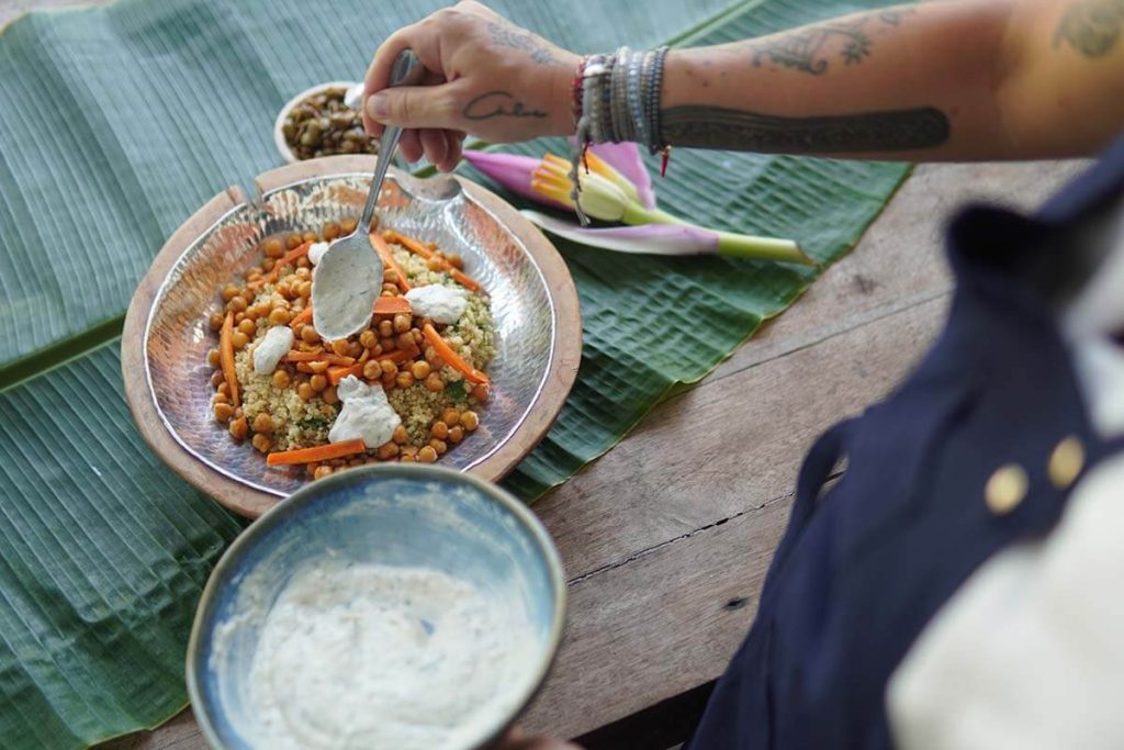 A quinoa salad topped with chickpeas, carrots, and a dollop of yogurt, served on a wooden table.