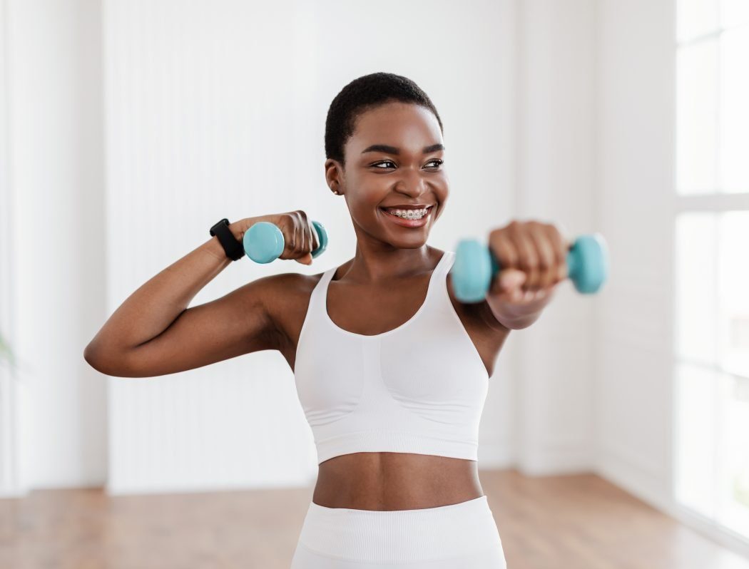 Black Lady Exercising with Dumbbells A woman with short hair holding light blue dumbbells while smiling during a workout session.