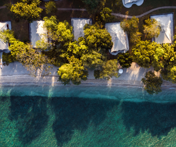 Aerial view showing beachfront tents surrounded by trees and clear water along the shoreline.