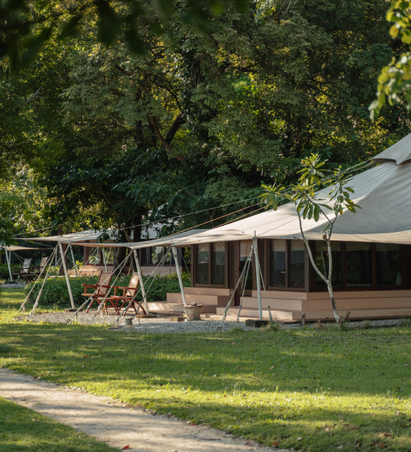 Canvas tent structure with a wooden deck and seating area in a natural outdoor environment.