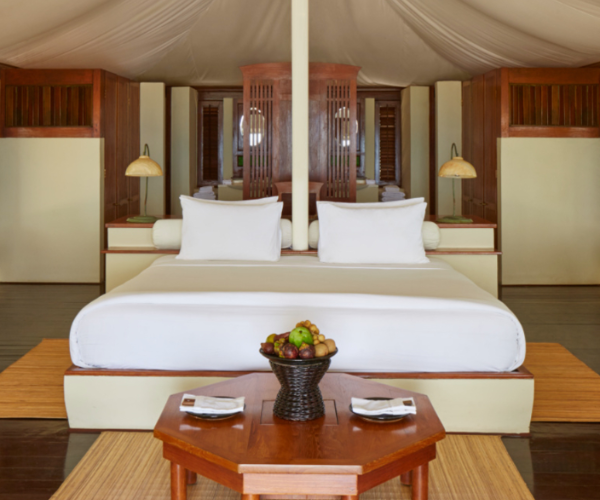 Interior of a luxury bedroom with a wooden table Luxury bedroom featuring a large bed with white linens and a wooden table with a fruit basket.