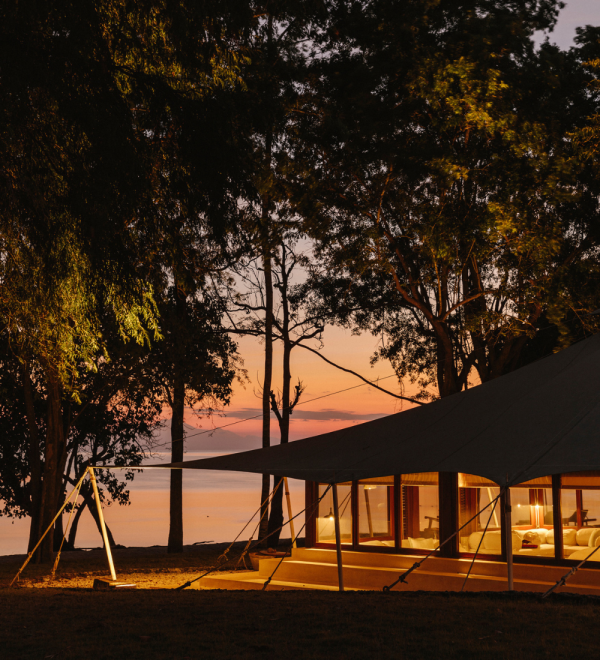Tent accommodation with a view of the sunset, surrounded by trees and a calm body of water.