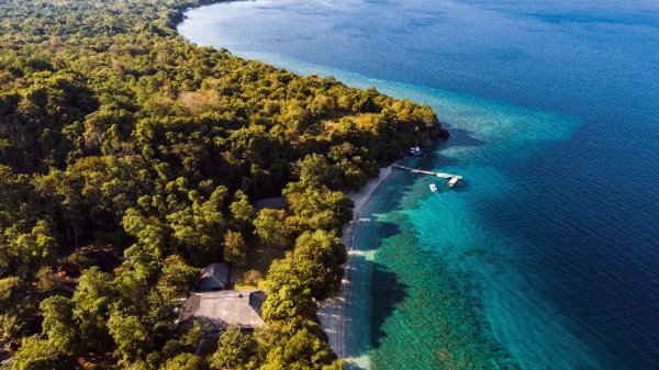 Aerial view of a coastal landscape featuring clear blue water and lush greenery along the shoreline.