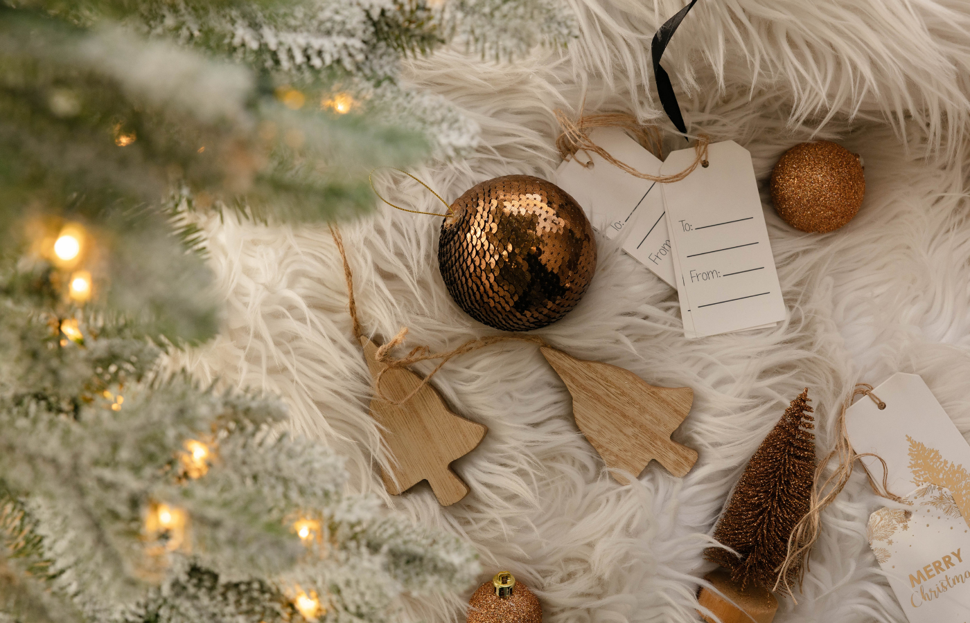Christmas Decorations and Gift Tags Decorative Christmas ornaments including a golden ball, wooden tree shapes, and gift tags on a fluffy white surface.
