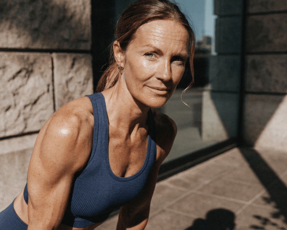 Athlete with toned arms wearing a blue sports top, posing outdoors in natural light.