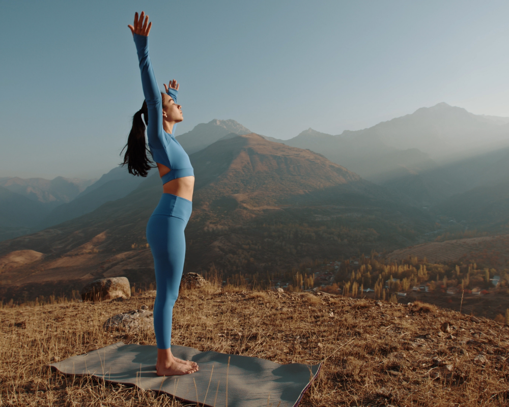 Woman performing a yoga pose on an 8-inch mat in a mountainous landscape during sunrise.