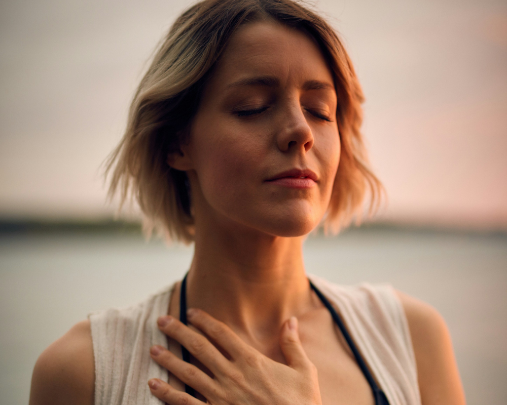 Woman with short hair and closed eyes, gently resting her hand on her chest in a serene expression.