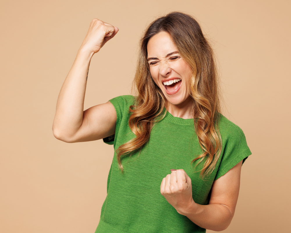 A dynamic brown-haired figure in a green top clenches a raised fist and shouts against a warm beige background, reflecting the Success Paradox and burnout.