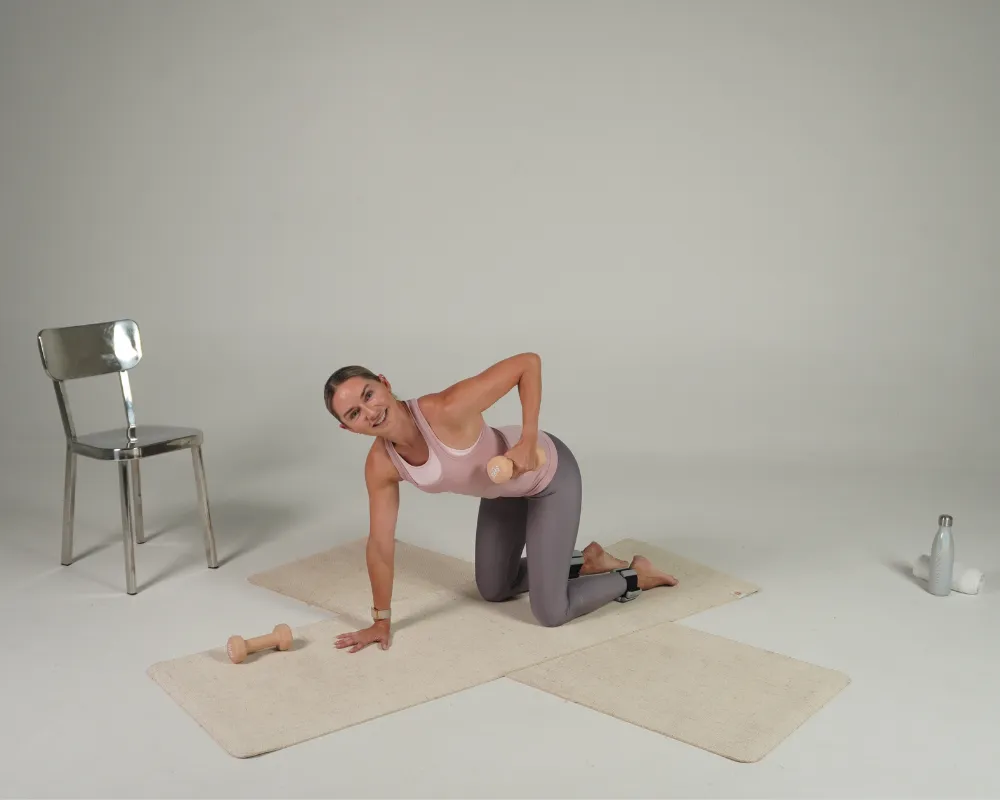 In a bright studio, a person in a pink top and grey leggings holds a grounding exercise on two yoga mats, reflecting on burnout and recovery.