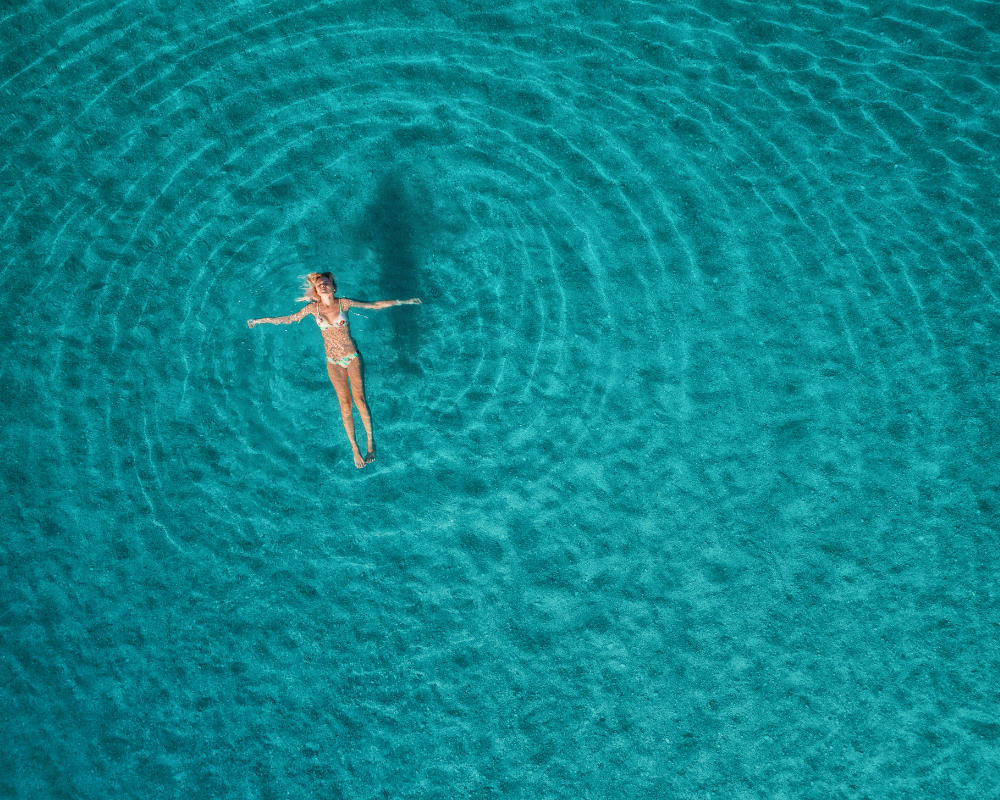Overhead view of a swimmer in clear turquoise ocean water, echoing restoration and recalibration themes from Silver Linings Wellbeing’s The Pause.
