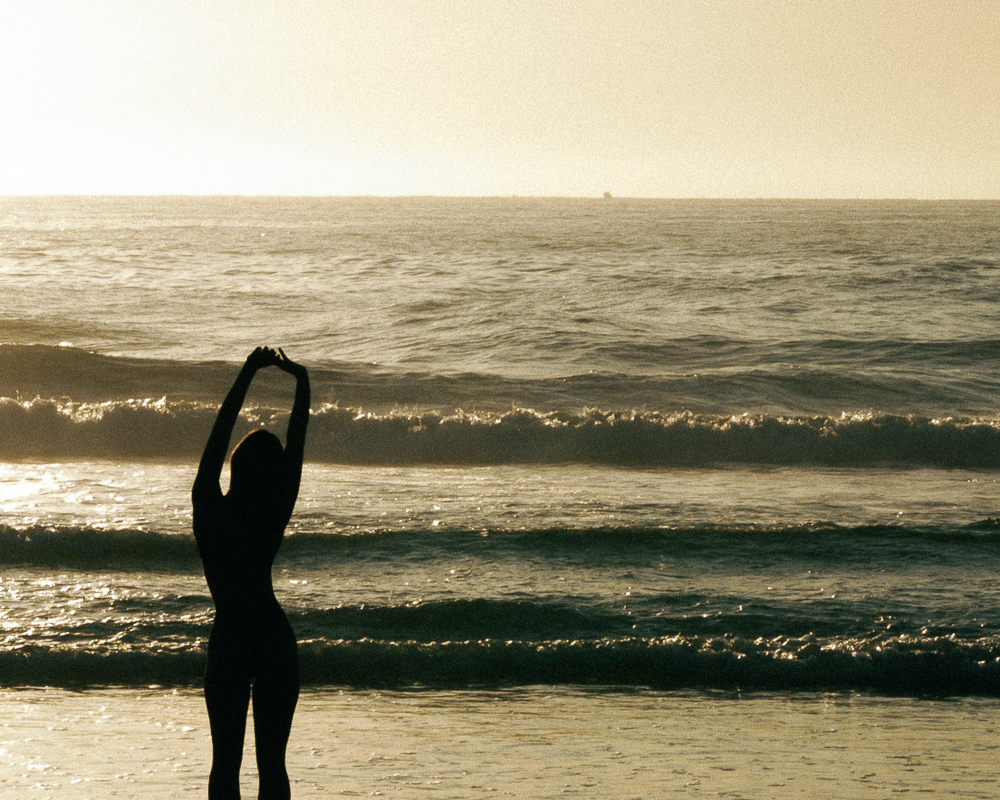 A dark silhouette stretches arms near the ocean horizon in golden light, echoing the idea of resetting your state beyond the scenery.